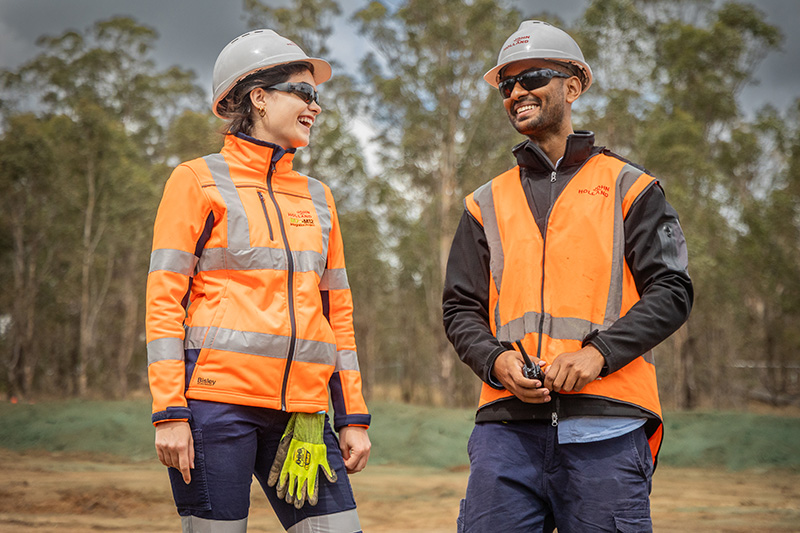 Two construction workers wearing high visibility vests with John Holland's logo on them